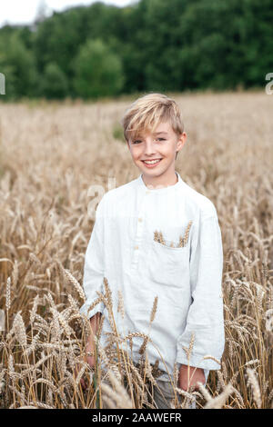 Portrait of happy blond boy standing in an oat field