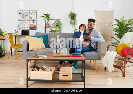 Multiethnic couple spending time together at living room and using smartphone Stock Photo