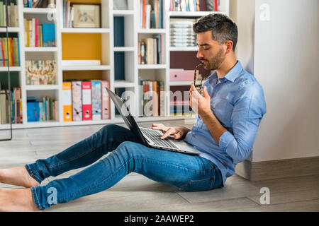 Young man sitting on the floor at home using laptop Stock Photo