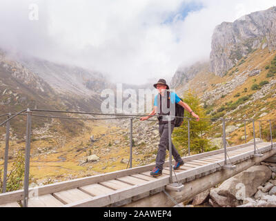 Hiker walking over a footbridge in the mountains, nature park Adamello, Italy Stock Photo