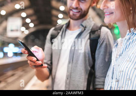 Young couple waiting for the train at the station and using smartphone, Berlin, Germany Stock Photo