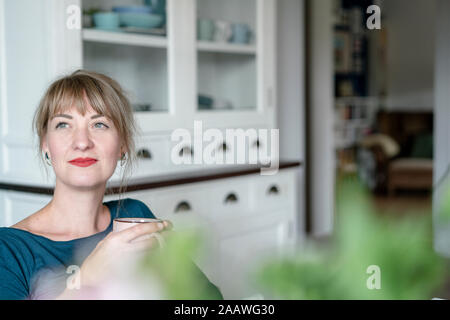 Portrait of woman with cup of coffee in the kitchen looking at distance Stock Photo