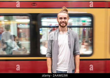 Young man at train station with blurred train as background Stock Photo