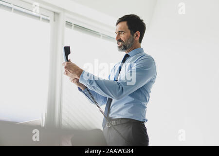 Angry mature businessman holding telephone receiver in office Stock Photo