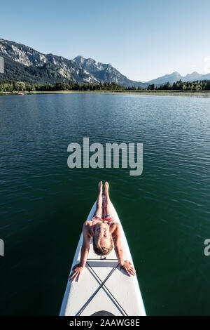 Girl sitting on SUP board and looking at camera, from above, Lake Bannwaldsee, Germany Stock Photo