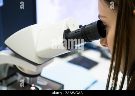 Young woman examining samples with microscope while working in modern laboratory Stock Photo