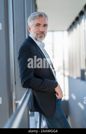 Portrait of mature businessman leaning on railing in a passageway Stock Photo