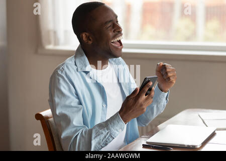 Overjoyed african American man feel excited using cellphone Stock Photo