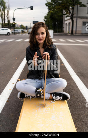 Portrait of smiling young woman with skateboard sitting on bollard Stock Photo