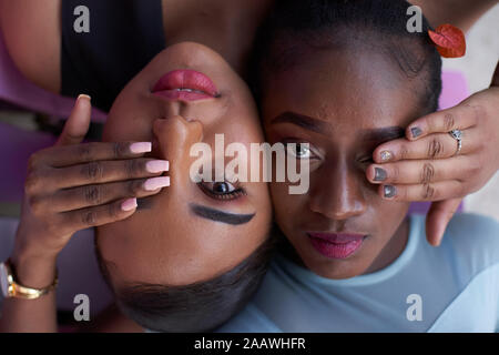 Portrait of two young women head to head covering eyes with hands Stock Photo