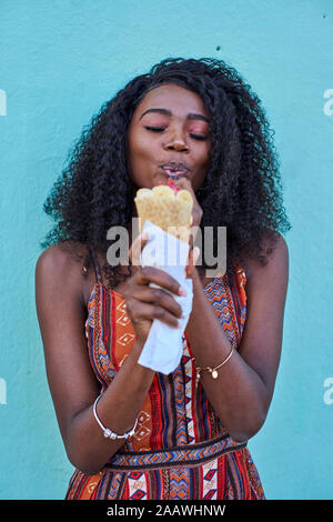 Portrait of young woman enjoying ice cream against blue wall Stock Photo