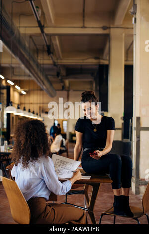 Two happy young businesswomen with smartphone in loft office Stock Photo
