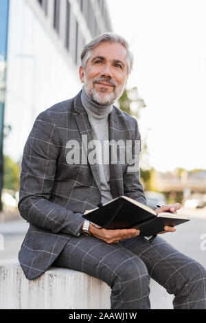 Fashionable mature businessman in the city sitting down with notebook Stock Photo