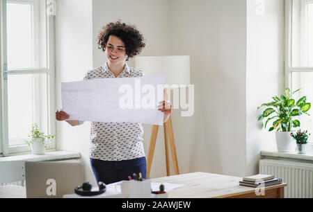 Smiling young woman studying a plan in office Stock Photo
