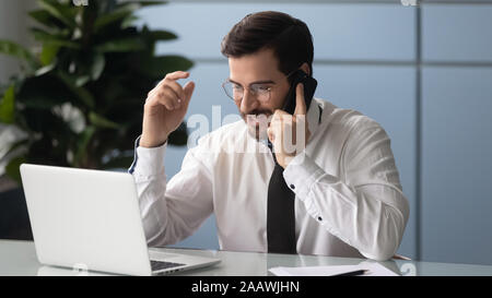 Young businessman talk on cell using laptop in office Stock Photo