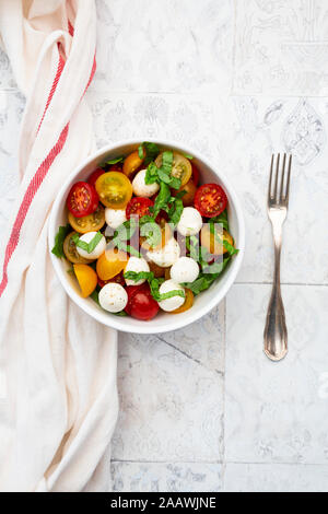 Napkin, single fork and bowl of fresh salad lying on tiled table Stock Photo