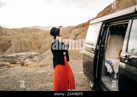 Young woman in desert landscape standing next to camper van, Almeria, Andalusia, Spain Stock Photo