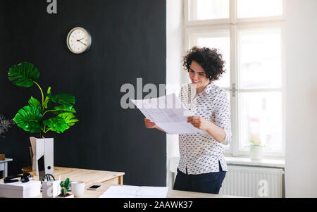Smiling young woman studying a plan in office Stock Photo