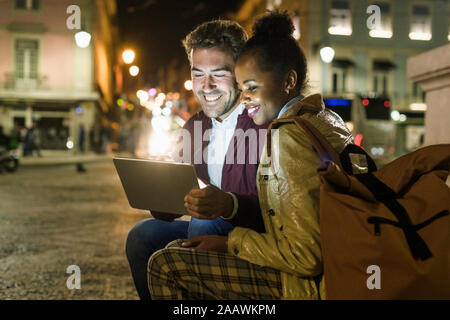 Portrait of happy young couple using digital tablet in the city by night, Lisbon, Portugal Stock Photo