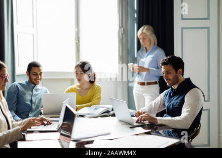 Colleagues disussing project, while mature woman is using smartphone in background Stock Photo