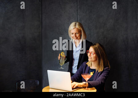 Colleagues discussing work, using laptop, drinking after work cocktails Stock Photo