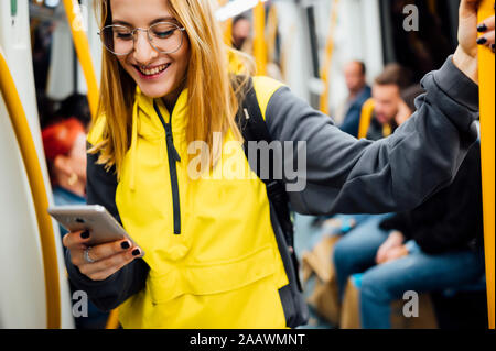 Smiling young woman standing in underground train using her smartphone Stock Photo