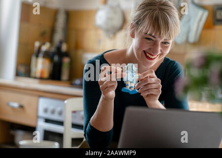 Portrait of laughing woman with little robot and laptop in the kitchen Stock Photo