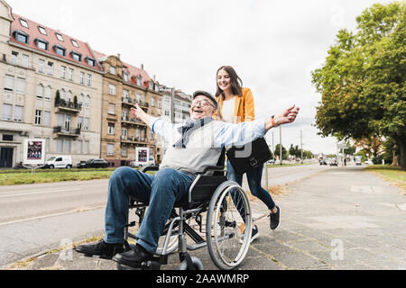 Smiling young woman pushing happy senior man in wheelchair Stock Photo