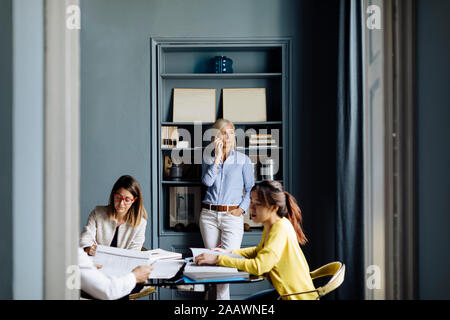 Woman talking on the phone, while colleagues having a project meeting Stock Photo