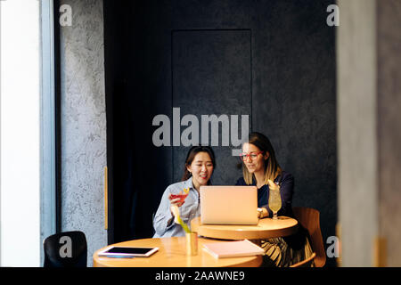 Colleagues discussing work, using laptop, drinking after work cocktails Stock Photo