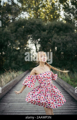 Portrait of happy young woman wearing summer dress with floral design dancing on boardwalk Stock Photo