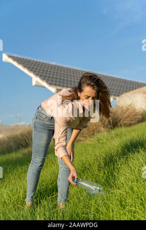 Woman on a meadow picking up empty plastic bottle Stock Photo