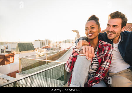 Happy affectionate young couple sitting on rooftop in the evening Stock Photo