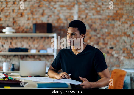 Young man sitting at table thinking Stock Photo