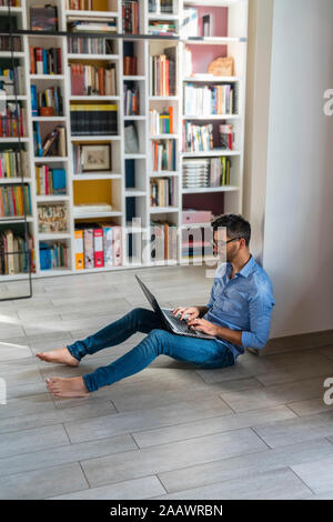 Barefoot young man sitting on the floor at home using laptop Stock Photo