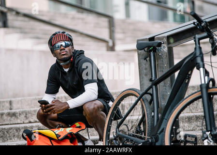 Stylish young man with bicycle, smartphone and messenger bag in the city Stock Photo