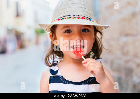 Portrait of smiling little girl with heart-shaped lollipop in summer Stock Photo