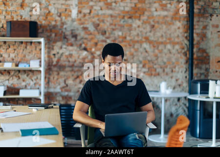 Young man sitting on chair using laptop Stock Photo