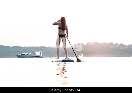 Back view of young woman stand up paddle-boarding at sunset, Lake Starnberg, Germany Stock Photo