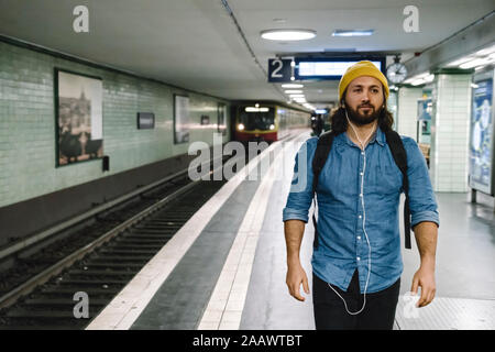 Portrait of man with backpack and earphones walking at platform, Berlin, Germany Stock Photo