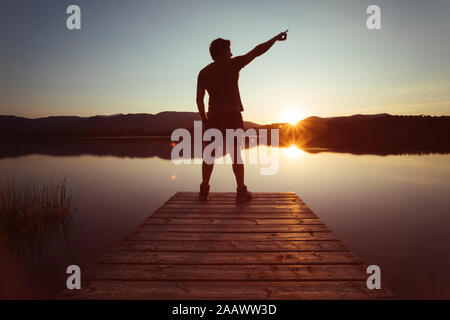 Silhouette of a man pointing to the sky on a wooden walkway at sunset Stock Photo