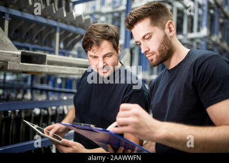 Two workers with clipboard and tablet in factory warehouse Stock Photo