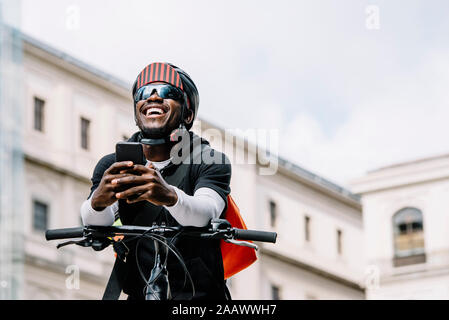 Happy stylish young man with bicycle, smartphone and messenger bag in the city Stock Photo