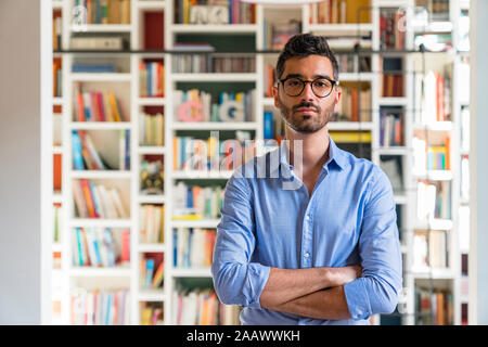 Portrait of bearded young man standing in front of bookshelves at home Stock Photo