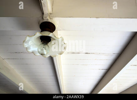 an incandescent lamp in the ancient glass lamp hang on the wooden beam under the second floor of an old wooden building Stock Photo