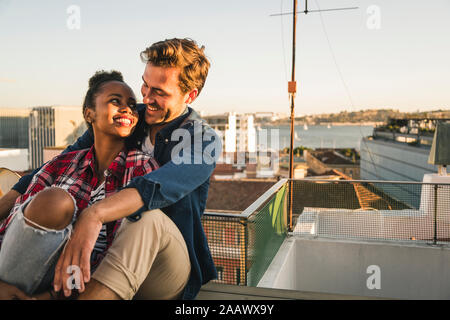 Happy affectionate young couple sitting on rooftop in the evening Stock Photo