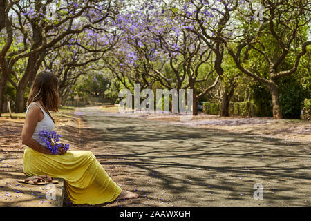 Woman holding jacaranda flowers in the street, Pretoria, South Africa Stock Photo