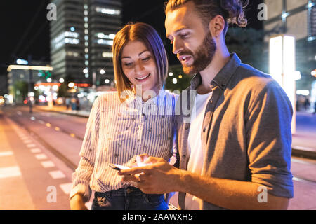 Happy couple in the city at night checking on their phones, Berlin, Germany Stock Photo