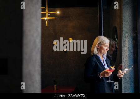 Mature businesswoman taking after work cocktail, using smartphone Stock Photo