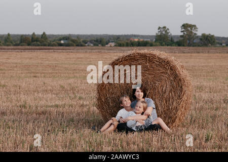 Woman with two kids sitting near a haystack on a stubble field Stock Photo